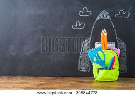 Back To School Concept With Small Bag Backpack, School Supplies And Rocket Sketch Over Chalkboad Bac