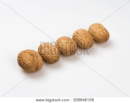 Five Walnuts (júglans Régia) On A White Background Lie In A Row Diagonally.