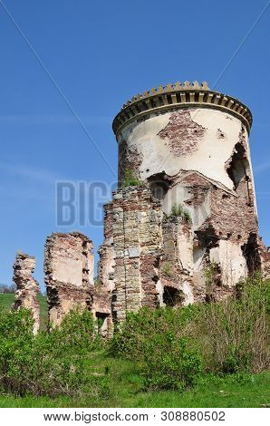 Old Ruined Stone Tower With Ruins Around. Green Thickets Of Grasses And Shrubs Under The Blue Sky. S