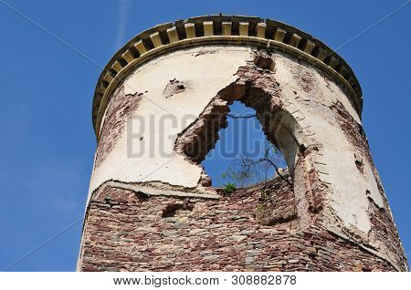 Old Destroyed Brick Tower With Falling Off Plaster Against The Blue Sky. From The Stone Walls Grows 