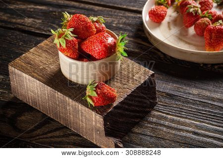 Ripe Strawberries In A Cup And On A Ceramic Plate Lie On A Wooden Background.