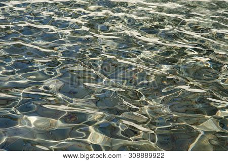 Sunny Water Light Ripples Over Grey Rocks.  Clear Water With Sunlit Ripple Patterns. Sun On Water Wi