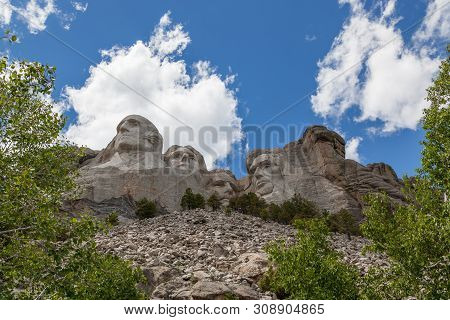 Blue Sky And White Fluffy Clouds Provide A Striking Back Drop For The Carved Faces Of Four Famous Un