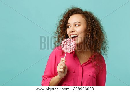 Young African Girl In Casual Clothes Holding, Eating Pink Round Lollipop, Looking Aside Isolated On 
