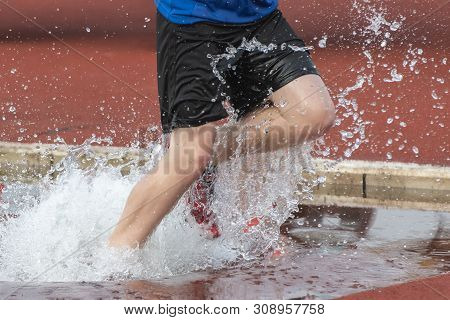 Runner Running Through The Steeple Chase Water Bake On A Running Track