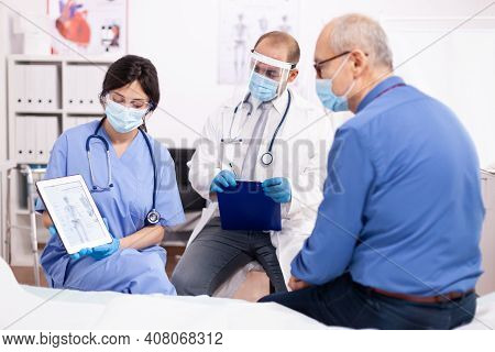 Doctor Discussing About Bone Disease With Senior Man Pointing At Tablet Pc In Cardiology Wearing Fac
