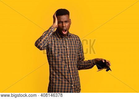 No Cash. Upset Black Guy Holding Empty Wallet And Touching Head In Frustration, Unemployed African A