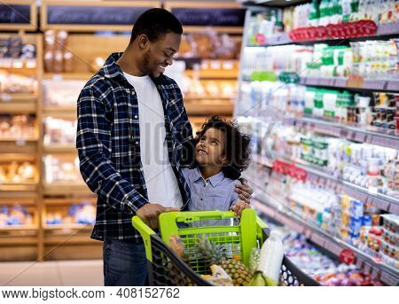 Happy Black Dad And His Pretty Little Daughter With Shopping Trolley Having Great Time Buying Grocer