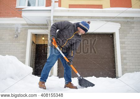 A Mature Man Clean Path Near House From Snow During Strong Blizzard. Person Shoveling Snow Out Of Th