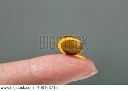Female Hand Holding A Small Yellow Capsule Of Nutritional Supplement . Food Supplement, Vitamin D, O