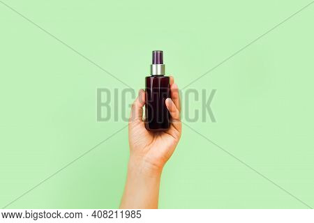 Male Hand Holds Unbranded Brown Plastic Spray Bottle On Pastel Green Background. Cosmetic Bottle Con