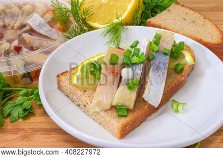 Open Sandwich Made Of Brown Bread, Slices Of Fillet Of Pickled Atlantic Herring, Fresh Lemon And Cho