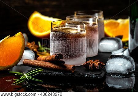 Frozen Herb Liqueur In Small Glass. Shot Glass Of Herb Liqueur With Cinnamon And Oranges On A Dark B