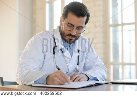Focused 35s Male Doctor Gp Physician Working With Registry Book.