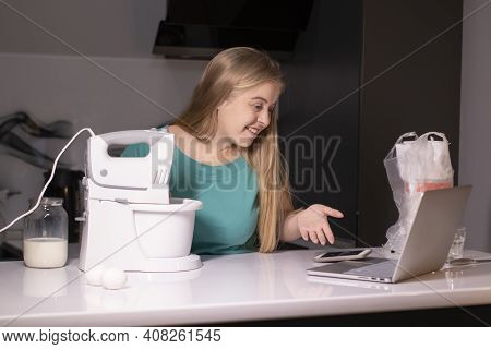 A Blonde Woman Videoblogger Cooking In Modern Kitchen Near Laptop, Online Learning Or Remote Cooking