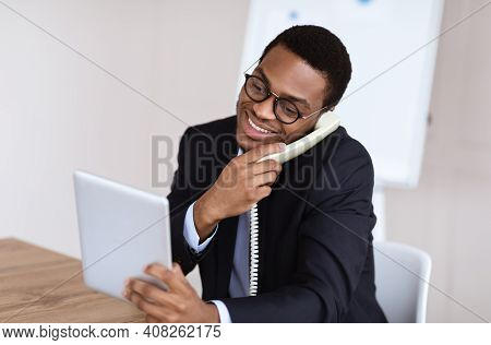 Happy Black Man In Suit Office Manager Or Businessman Talking On Phone, Using Digital Tablet At Work