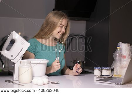 A Blonde Woman Videoblogger Cooking In Modern Kitchen Near Laptop, Online Learning Or Remote Cooking