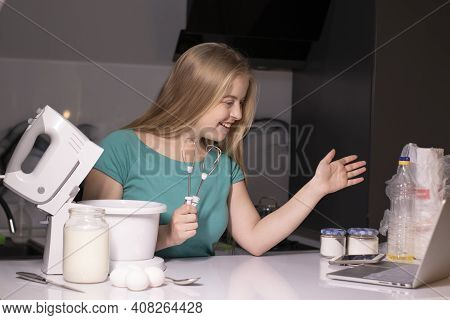 A Blonde Woman Videoblogger Cooking In Modern Kitchen Near Laptop, Online Learning Or Remote Cooking