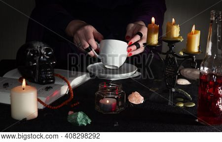 Fortune-telling On Coffee Grounds. A Fortune Teller's Hands, A Cup Of Coffee, Candles, And Skulls On
