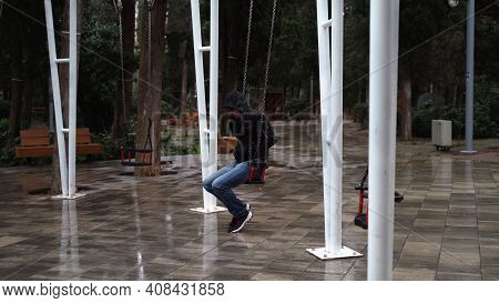 Lonely Man In The Park Swinging On A Swing. A Sad Man In Depression Is Lonely Swinging On A Swing In