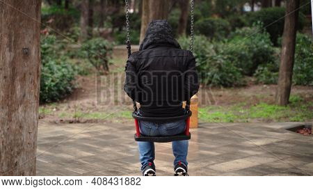 Lonely Man In The Park Swinging On A Swing. A Sad Man In Depression Is Lonely Swinging On A Swing In