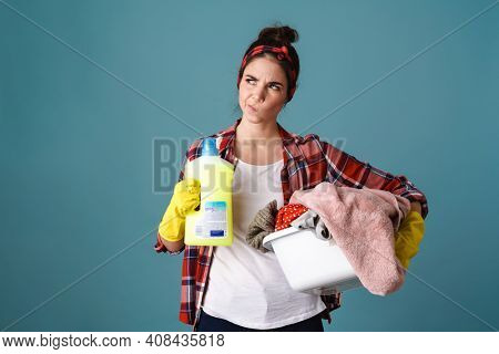 Upset housewife in apron and rubber gloves holding cleaning tools isolated over cblue