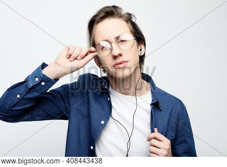 Happy young stylish man wearing casual and eyeglasses adjusting his headphones and smiling while standing against white background