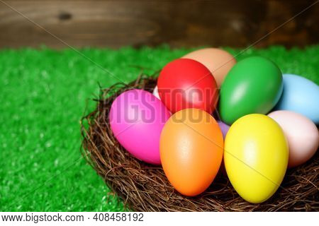 Multi Colored Easter Eggs In Birds Nest On Green Grass And Wooden Panks Background Closeup View Sele