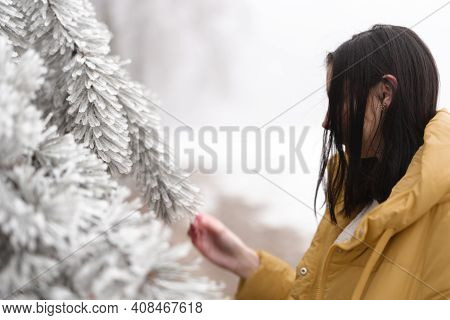 Girl In Winter With Orange Jacket Touching Frozen Tree Covered With Snow And Ice