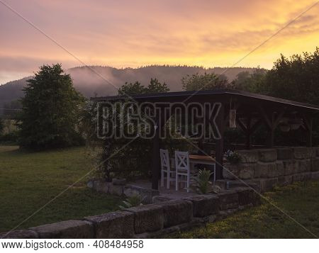 View Of Summer Garden With Tiber Wooden Gazebo Pergola With Blooming Climbing Plant Flowers And Whit