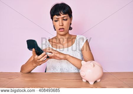 Beautiful brunettte woman caculating money savings clueless and confused expression. doubt concept. 