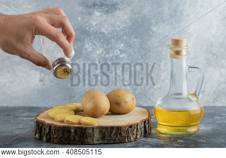 Man Pouring Salt Bottle On Sliced Potatos
