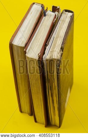 Three Old Dailies Standing On Endpaper On Yellow Background. The Diaries Have Worn Pages.