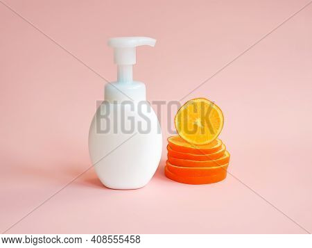 White Unbranded Bottle With Pump And Orange Slices  On Light Pink Background. Blank Container For Lo