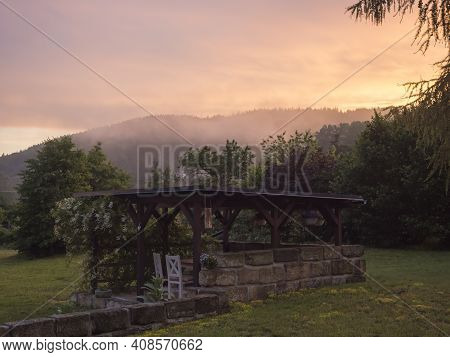 View Of Summer Garden With Tiber Wooden Gazebo Pergola With Blooming Climbing Plant Flowers And Whit