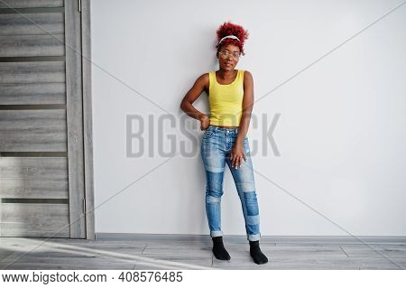 African American Woman In Yellow Singlet And Eyglasses Against White Wall.