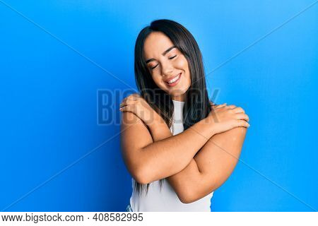 Young beautiful hispanic girl wearing casual clothes hugging oneself happy and positive, smiling confident. self love and self care 