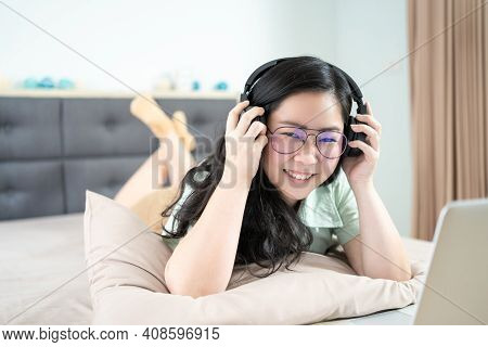 Beautiful Asian Woman Is Using A Headset With Laptop And Lying On The Bed In Her Bedroom With A Past