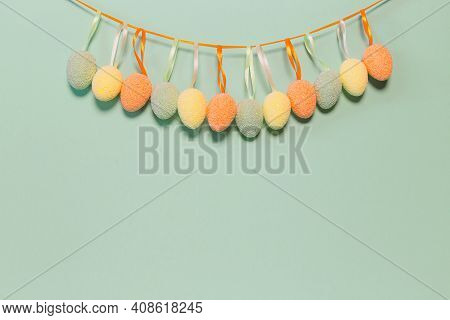 Decorative Easter Eggs Hanging On A Strip Next To Greenl Pastel Background. Holiday Backdrop For Sea