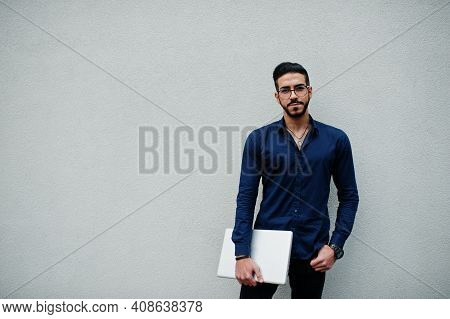 Middle Eastern Entrepreneur Wear Blue Shirt, Eyeglasses, Hold Laptop Against White Wall.