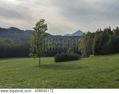 Meadow With Forest, Trees And Hills, Summer, Day, Moody Sky. Landscape In Luzicke Hory Lusatian Moun