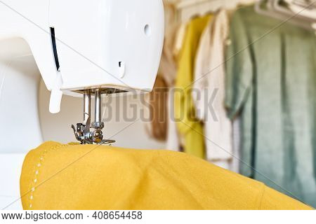 Close Up Of Sewing Machine With Yellow Linen Fabric And Linen Clothes On Background. Industry, Fashi