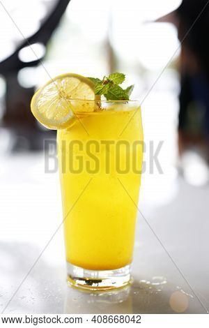A Close-up Of Glass Of Lemonade With Ice Cubes, Mint Sprig, Lemon Slice And A Pinch Of Turmeric. Yel