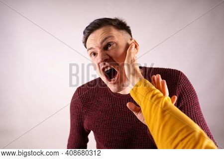 Crop Person Slapping Scared Man In Face. Emotional Male Getting Slapped In Face While Shouting With