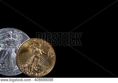 A One Ounce Gold Coin And A One Ounce Silver Eagle Coin On A Black Background, With Copy Space
