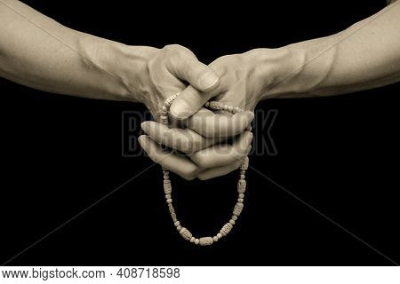 The Mans Sinewy Hands Are Clasped Together, Fingering A Rosary Against A Black, Isolated Background.