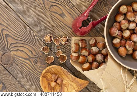 Hazelnuts With A Red Nutcracker In A Bowl On A Wooden Board, Nutshell, Dark Photo, Flat Lay
