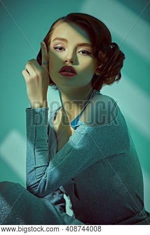 Art fashion portrait of a beautiful young woman in evening dress stands in the shade of the window. Hair and makeup in the style of the 20s. 