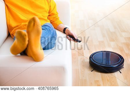 Man Resting While Robotic Vacuum Cleaner Doing Chores, Clean Work At Home. Man Controls A Robot Vacu