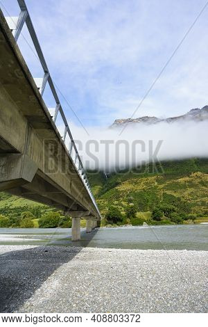 Bridge And Shadow Across Stony Scenic River Bed Of Dart River At Te Araroa Trail Bridge In Otago New
